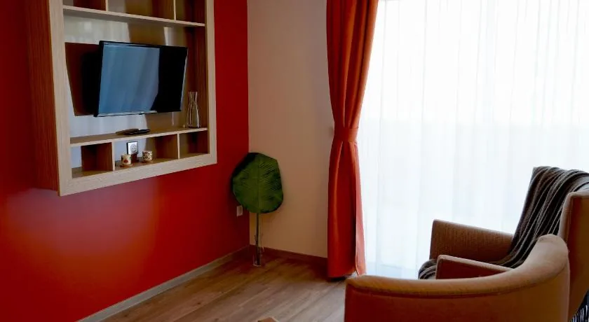 Lounge area: TV recessed into a red wall, armchair and curtains, Appart-One aparthotel, Uzès